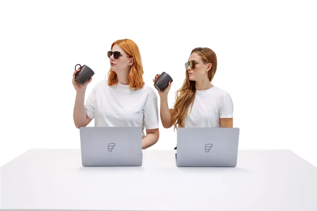Bild von zwei Personen die an einem Computer arbeiten und dabei mit einer Kaffeetasse in der Hand in die selbe Richtung schauen